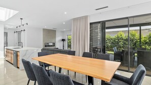 A modern kitchen with a marble countertop, a dining area with a wooden table and grey chairs, and a large sliding glass door leading to an outdoor patio.