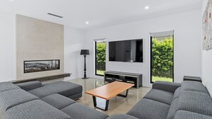 A modern living room with grey sofas, a wooden coffee table, a flat-screen TV, and a fireplace.