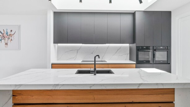 A modern kitchen with a marble countertop, a sink, and built-in ovens.