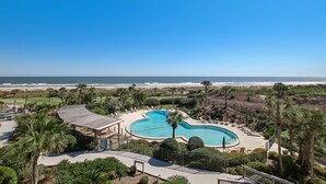 Um resort com uma piscina grande, palmeiras e vista para a praia.