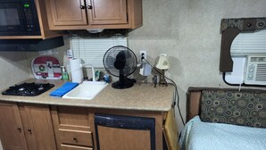 A compact kitchen with a microwave, stove, sink, and a fan. - Cozy RV in amazing Austin with AC, WiFi, Swimming Pool (Austin)