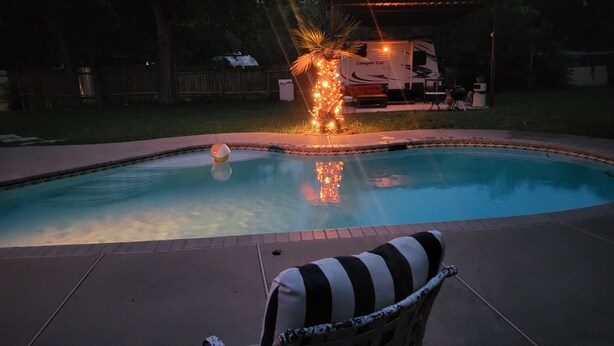 A swimming pool with a small waterfall feature, surrounded by a patio area with a chair. - Cozy RV in amazing Austin with AC, WiFi, Swimming Pool (Austin)