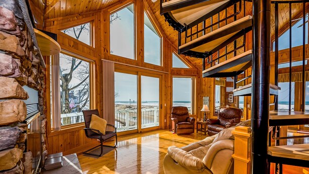 A spacious wooden interior with large windows, a stone wall, and a cozy seating area with leather chairs and a sofa. - Sunset Kisses. Beachfront Luxury vacation rental (South Haven)
