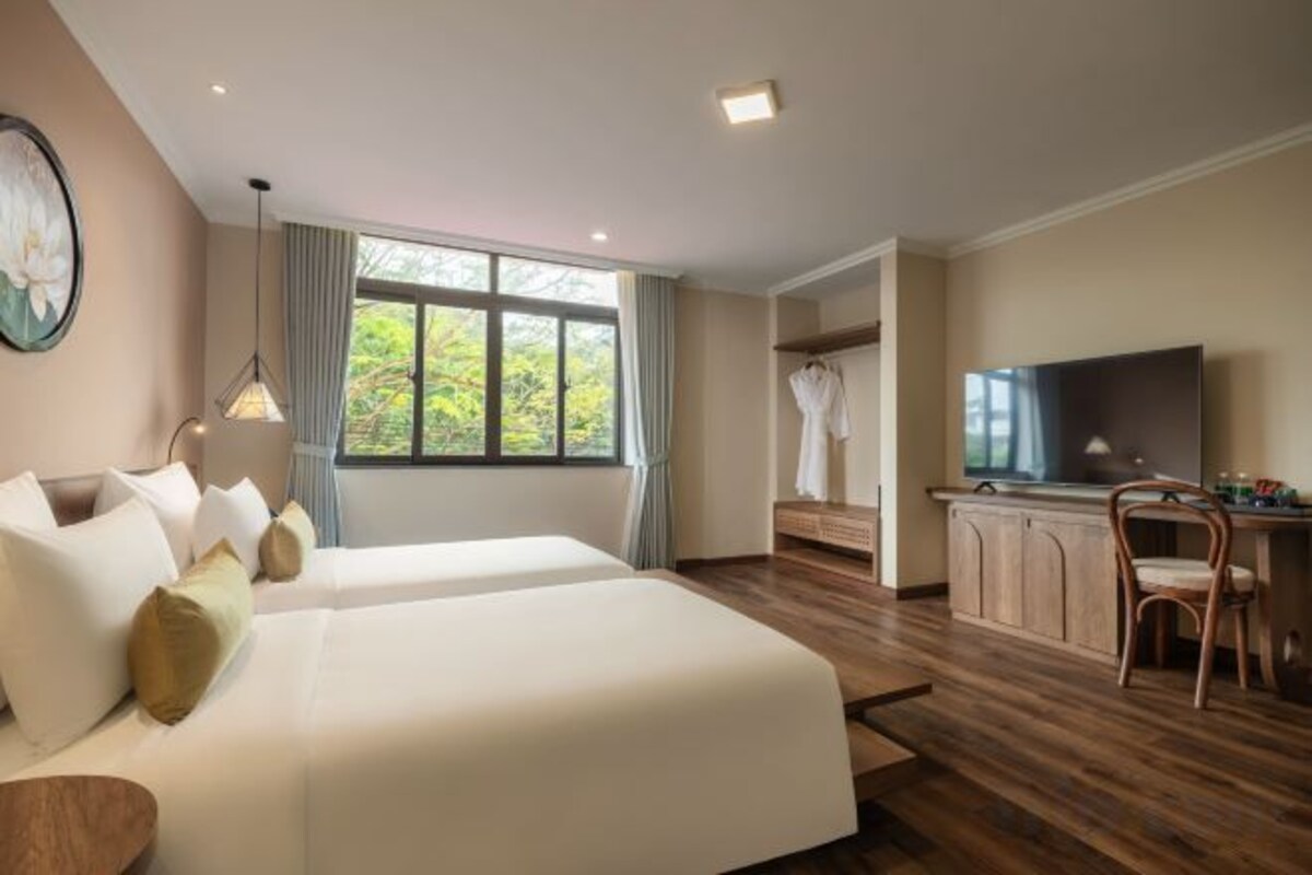 A hotel room with a large bed, a desk with a chair, a television, and a window with curtains.