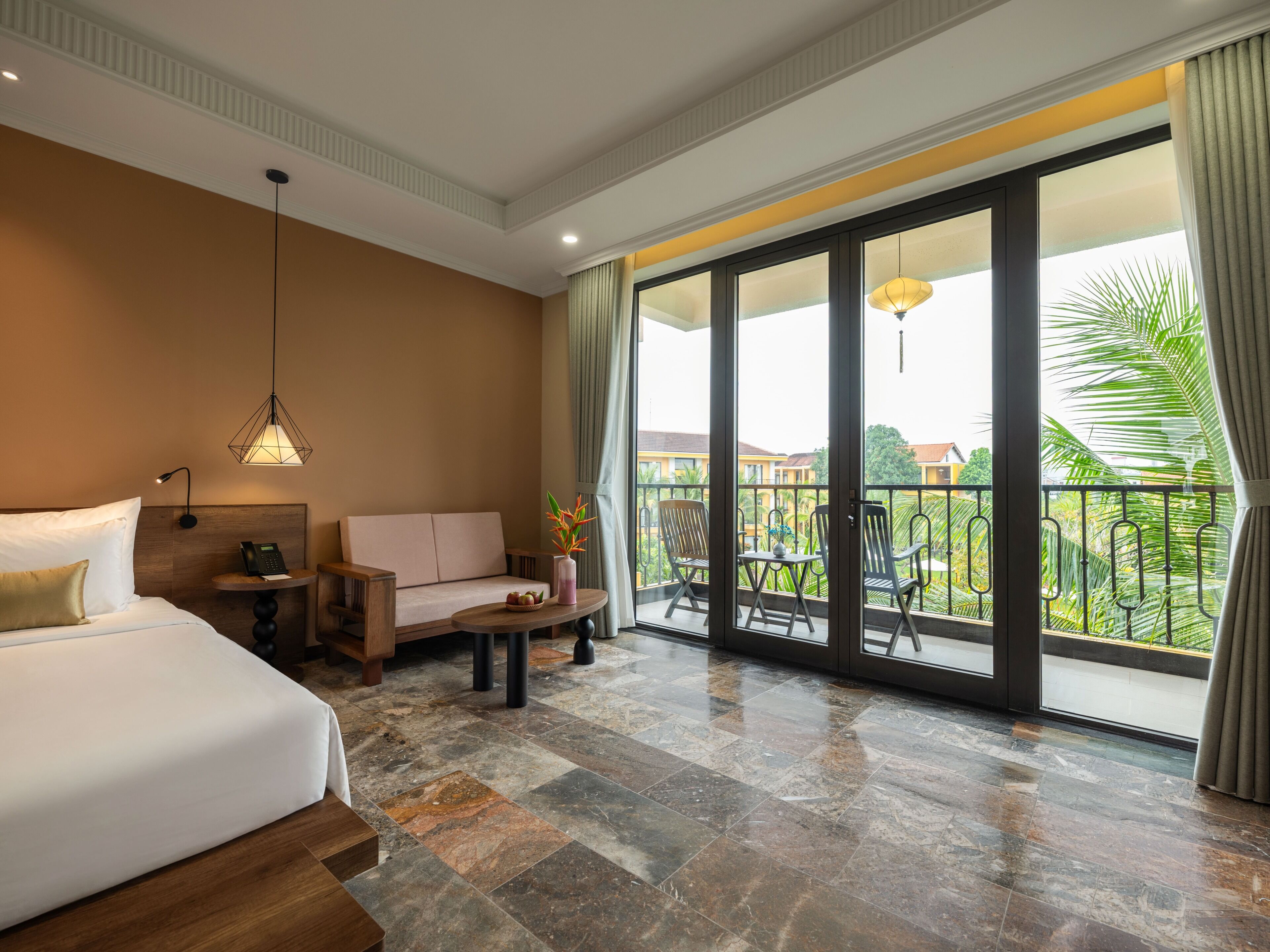 A hotel room with a bed, a sofa, a small table, a phone, and a balcony with a view.
