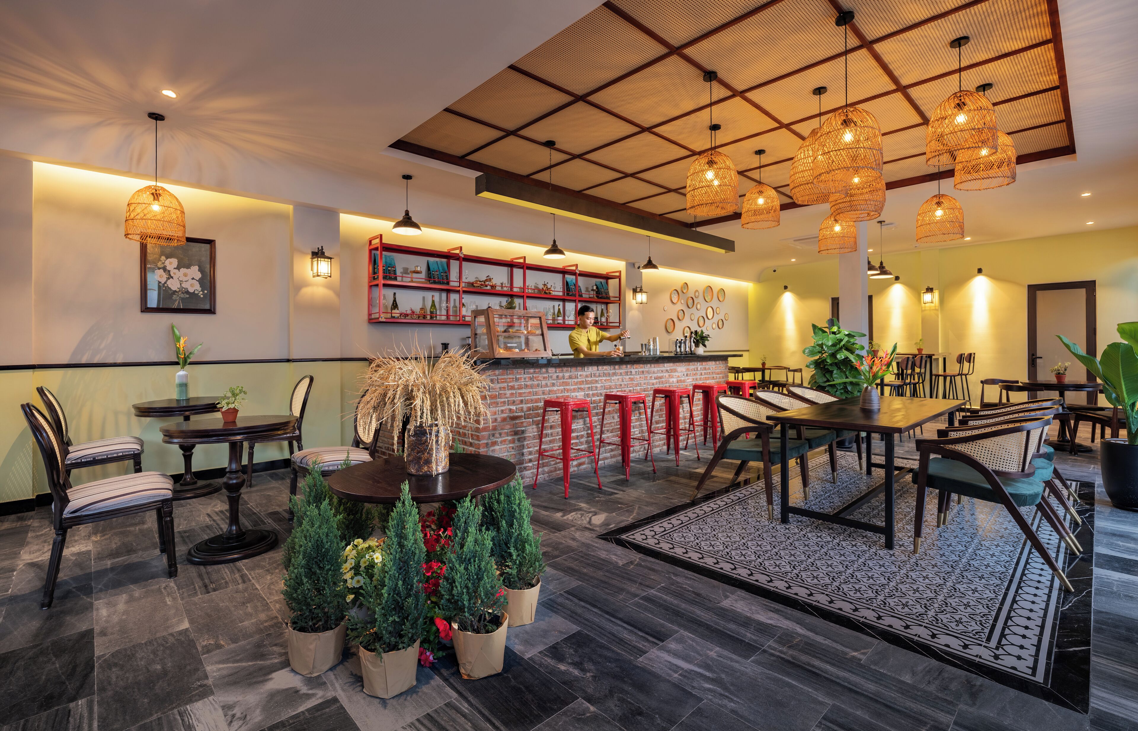 A restaurant with a bar area, round tables, red bar stools, and hanging wicker lamps.