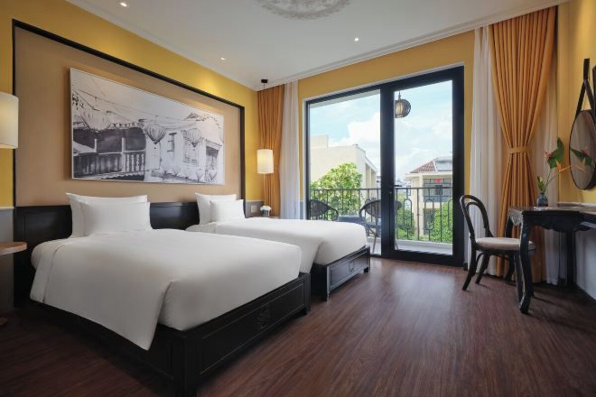 A hotel room with two beds, a large window with a balcony, and a painting on the wall.