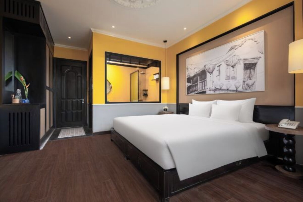 A hotel room with a large bed, a mirror, a painting on the wall, and a small table with a lamp.