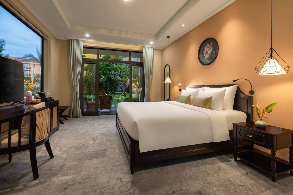 A hotel room with a large bed, a desk with a TV, a chair, and a view of the outdoors.