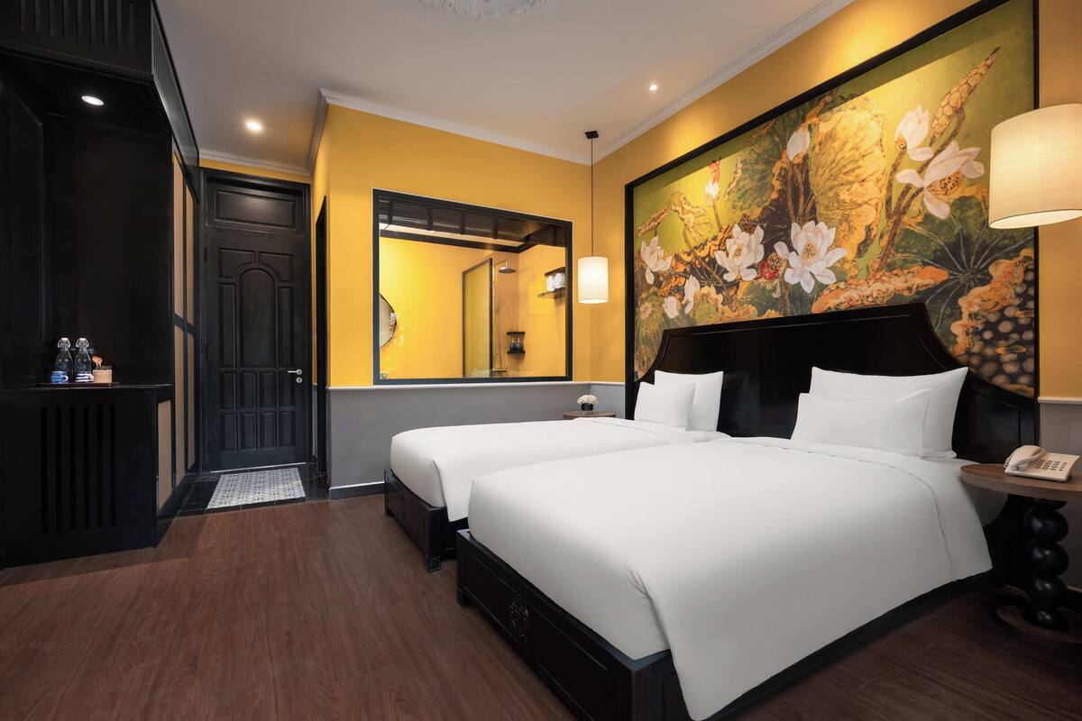 A hotel room with two beds, a large mirror, a painting of flowers, and a telephone on the nightstand.