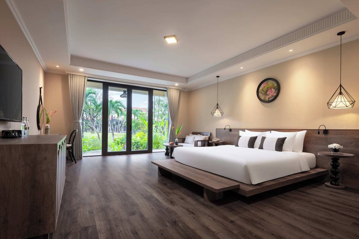 A spacious bedroom with a large bed, a desk, and a view of a lush garden through the sliding doors.