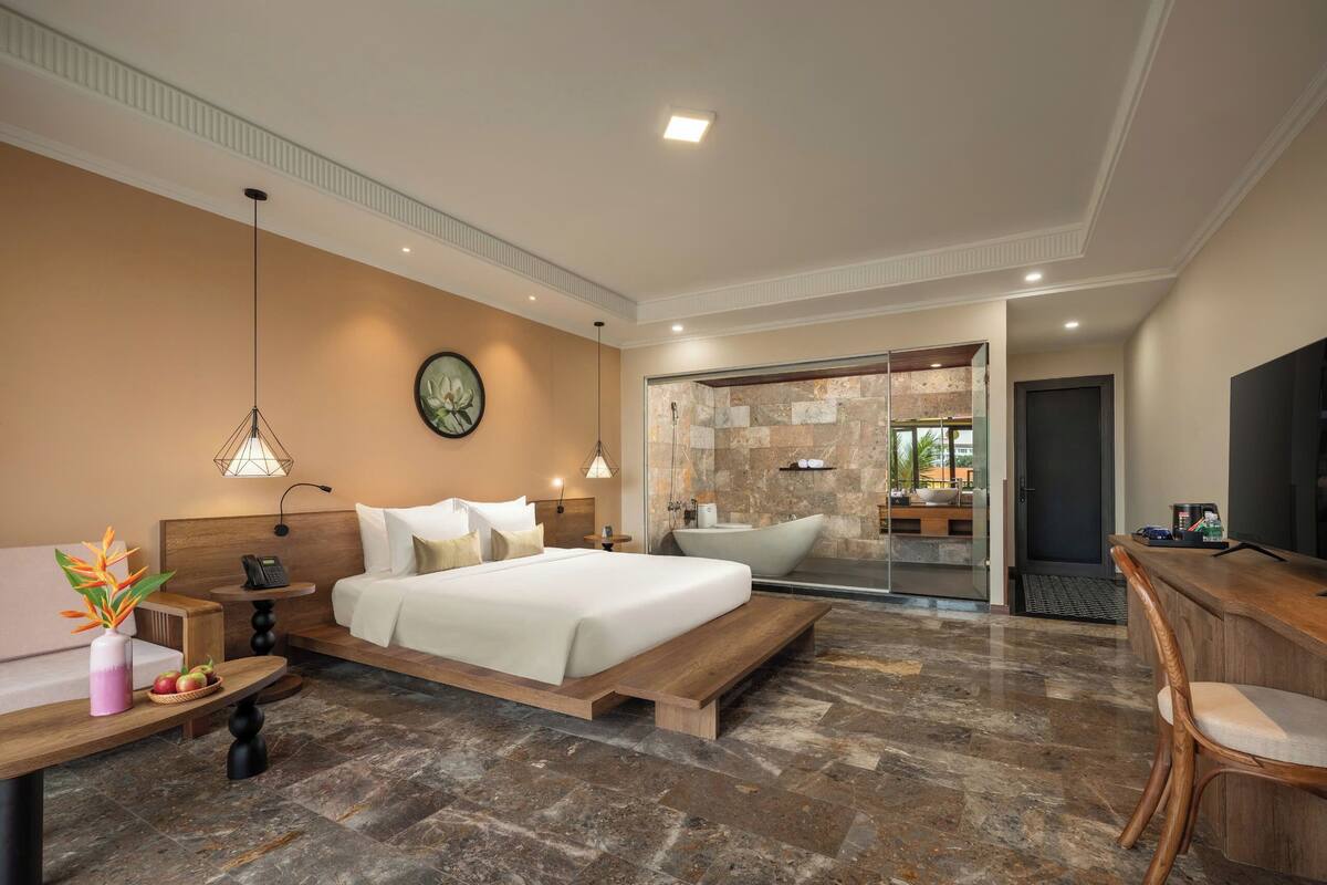 A modern hotel room with a large bed, a desk, a bathroom with a bathtub, and a TV.