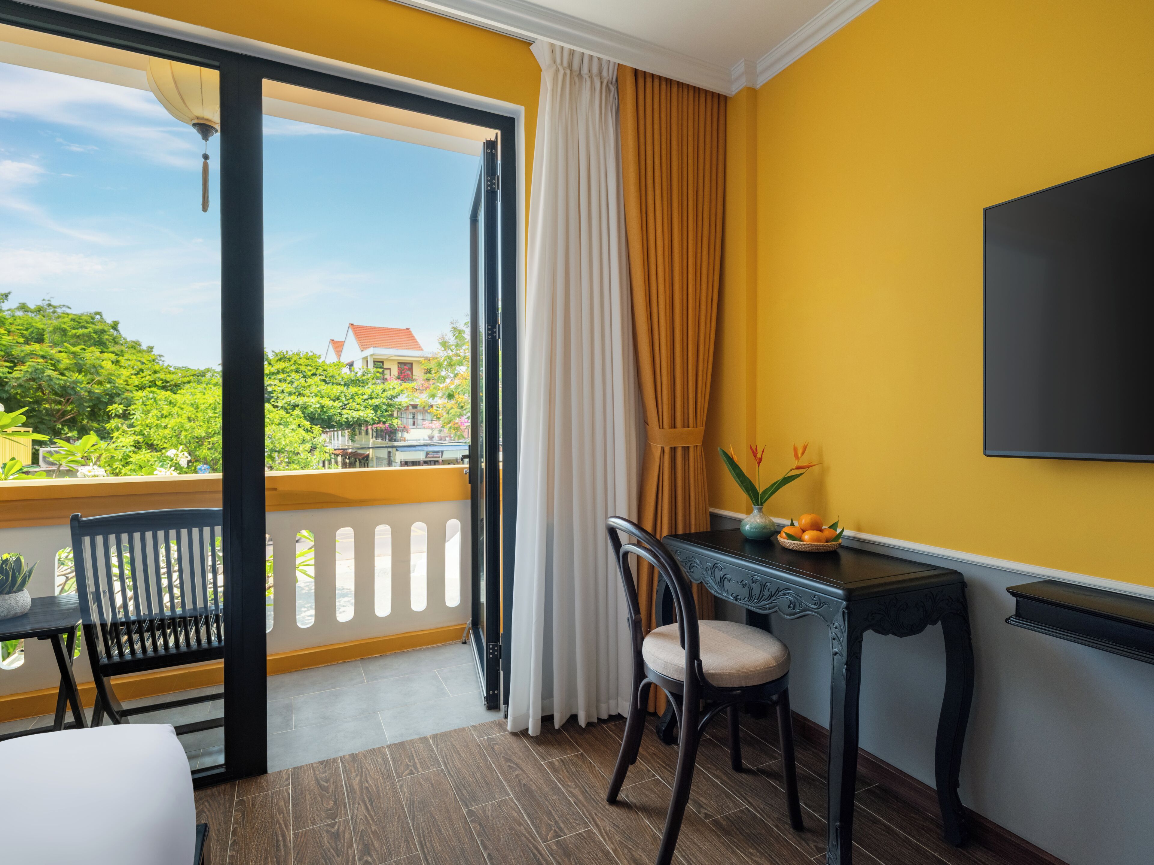 A room with a balcony, a dining table with chairs, a TV, and a window with curtains.