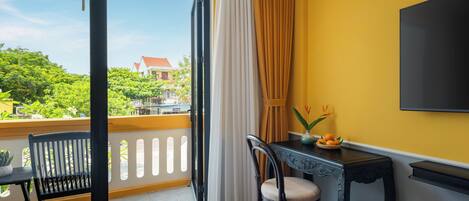 A room with a balcony, a dining table with chairs, a TV, and a window with curtains.