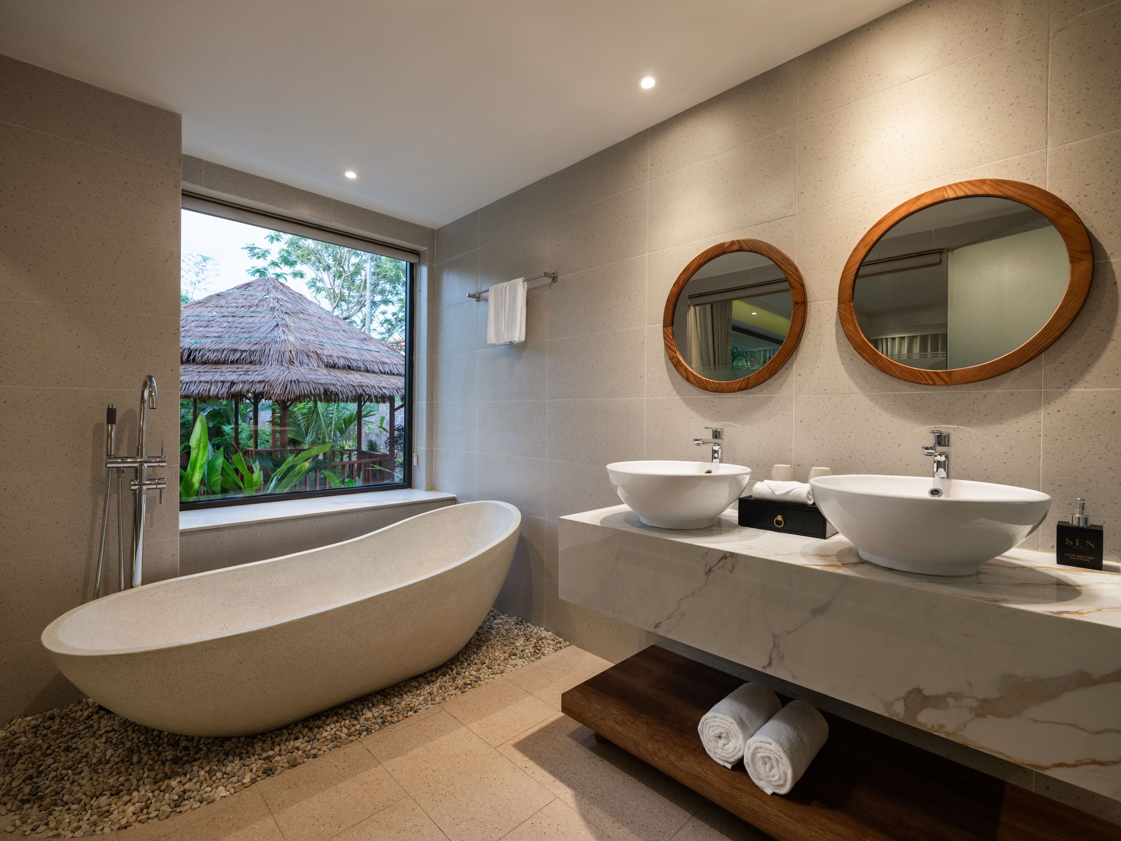 A modern bathroom with a freestanding bathtub, two sinks, and a large mirror.