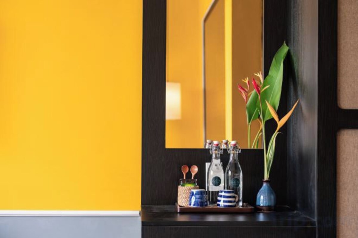 A bathroom with a yellow wall, a dark wooden vanity, a mirror, a vase with a plant, and a tray with toiletries.