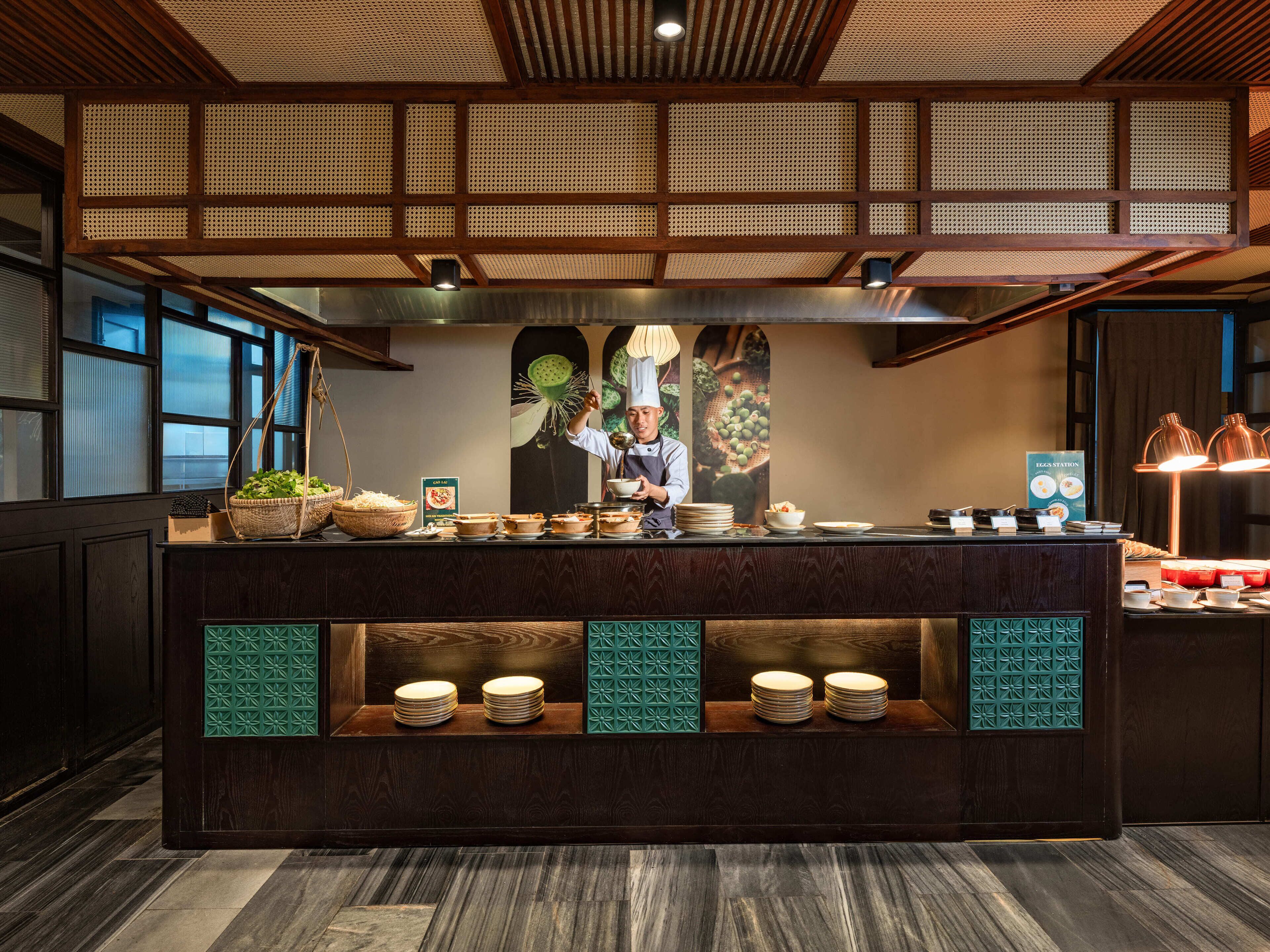 A restaurant interior with a chef preparing food, wooden ceiling, and a buffet counter with dishes.