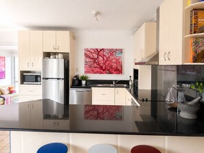 Een moderne keuken met een centraal eiland, roestvrijstalen apparatuur en een groot abstract schilderij aan de muur.