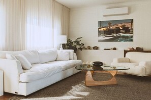 Un soggiorno moderno con un divano bianco, un tavolino in vetro e un quadro raffigurante una piscina.