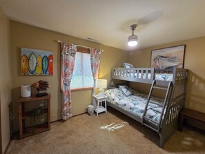 A bunk bed room with a ceiling fan, a small bedside table with a lamp, and a wall painting. - Misty Mare Townhouse - Gorgeous home on Chincoteague Island (Chincoteague)