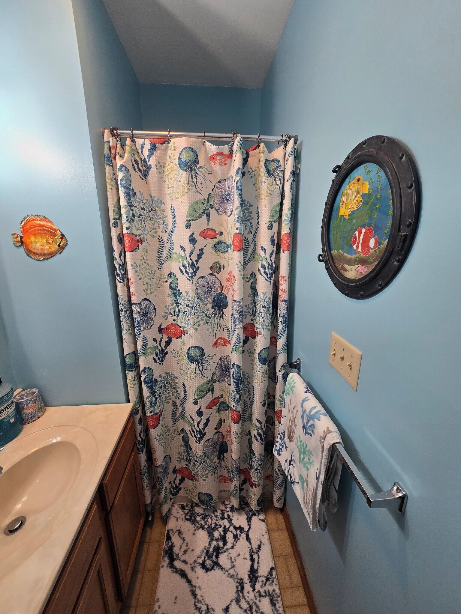 A bathroom with a shower curtain featuring a marine life pattern, a round window with a fish design, and a tiled floor.