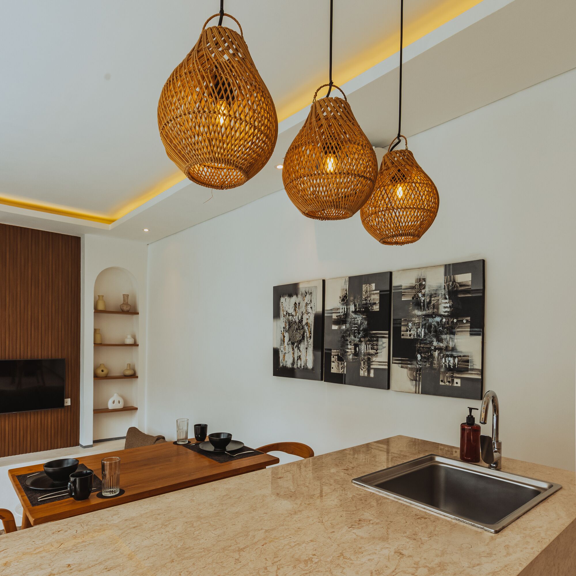 A modern kitchen with a central island, a built-in sink, and three woven pendant lights.