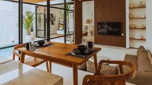 Una sala de estar moderna con una mesa de comedor de madera, asientos cómodos, un televisor de pantalla plana y vistas al exterior.