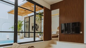 Una sala de estar moderna con un ventanal grande, un televisor de pantalla plana en la pared y una zona de estar acogedora con un sofá y una mesa de centro.