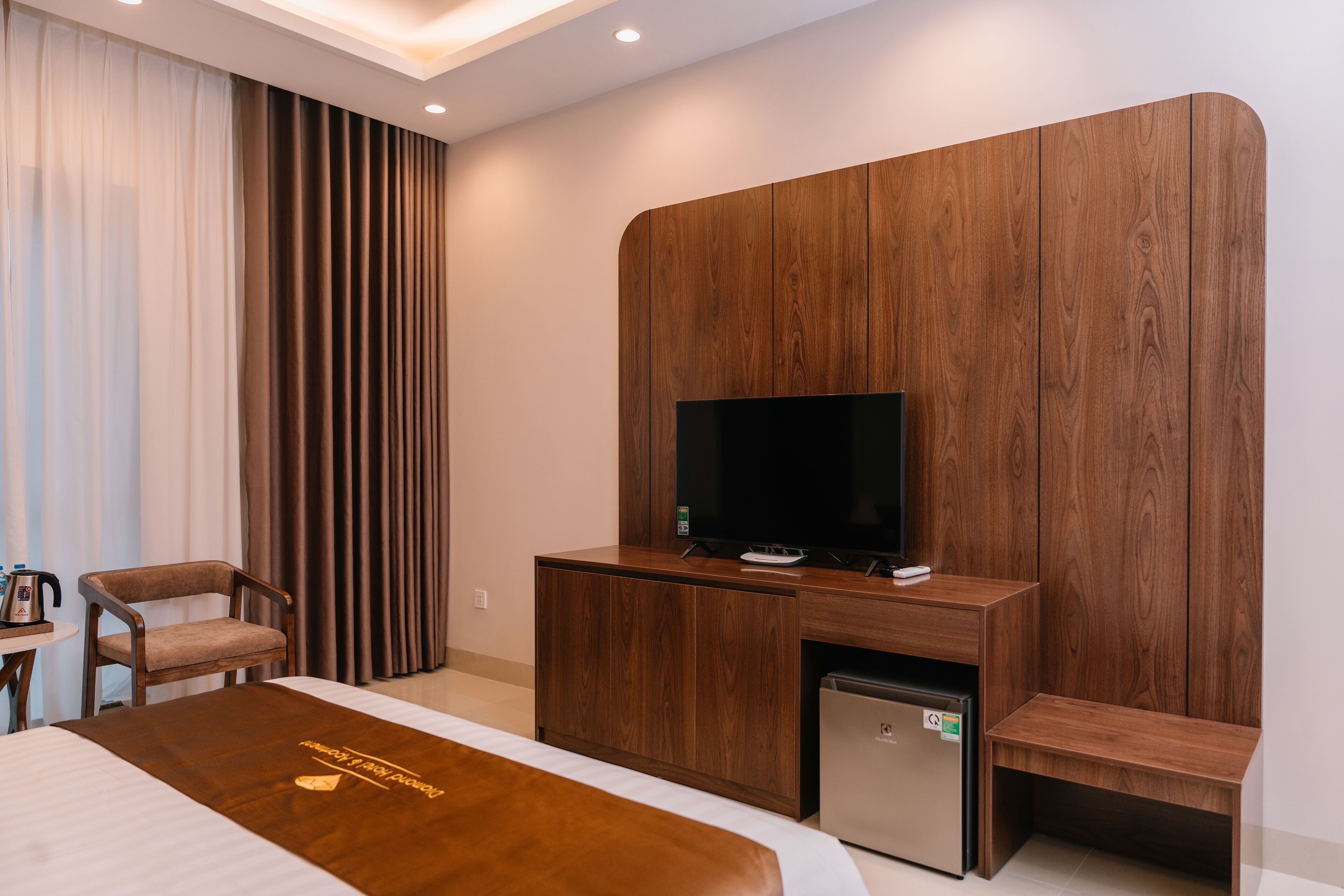 Une chambre d’hôtel moderne équipée d’un lit, d’un meuble en bois pour la télévision, d’un petit réfrigérateur et d’un coin salon.