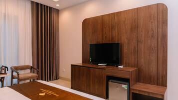 Une chambre d’hôtel moderne équipée d’un lit, d’un meuble en bois pour la télévision, d’un petit réfrigérateur et d’un coin salon.