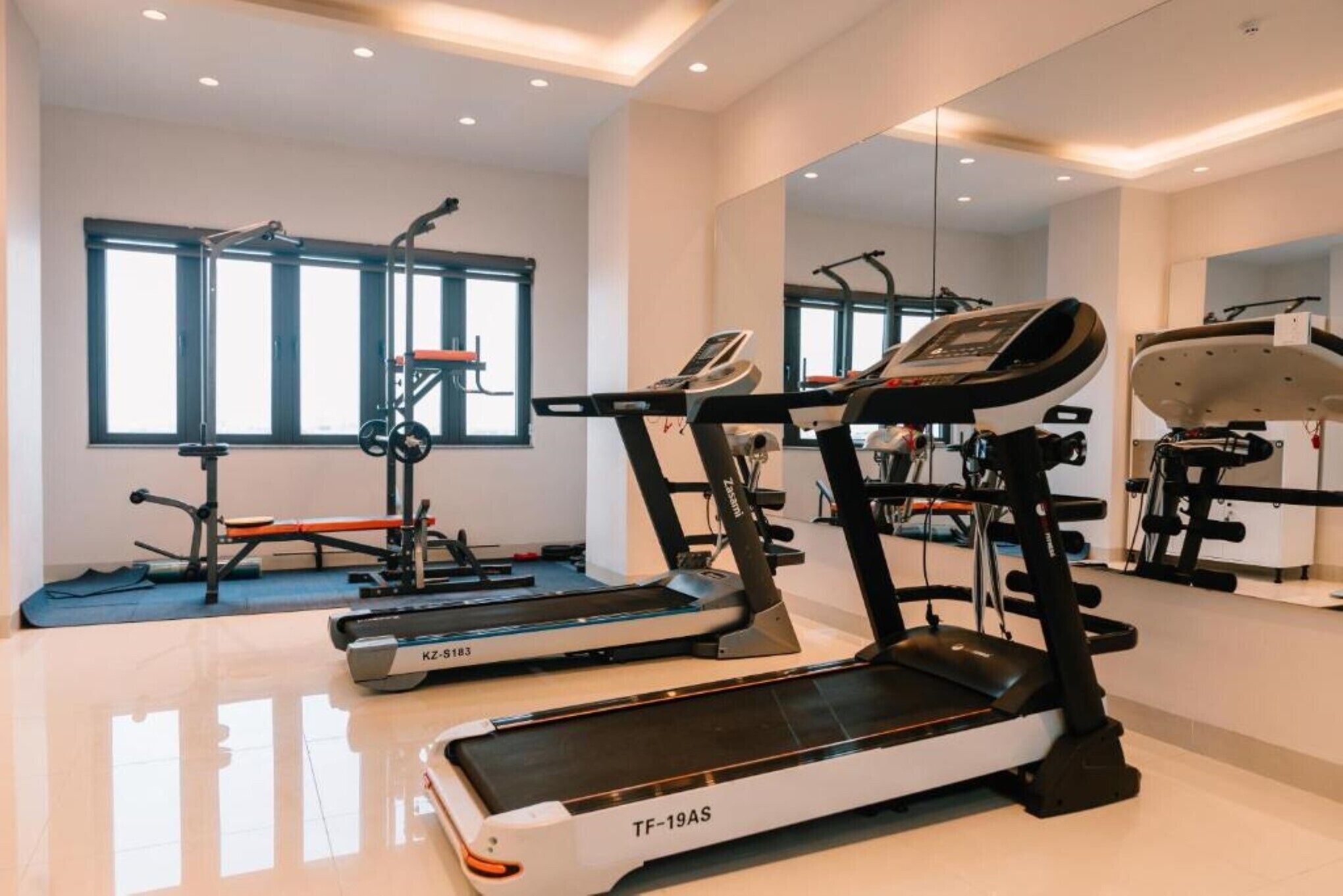 Et moderne fitnesscenter med løbebånd, styrkemaskiner og et spejl.
