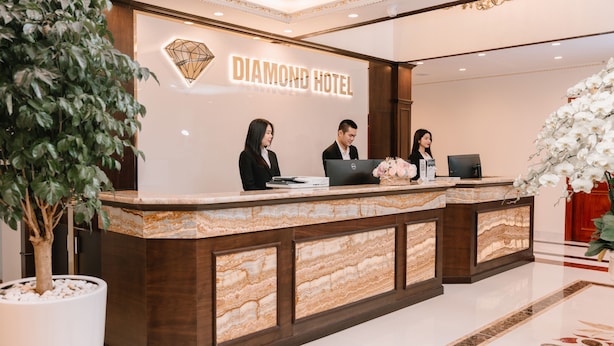 Un mostrador de recepción en el Hotel Diamond, con diseño de mármol, una planta en maceta grande y un letrero en la pared.