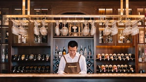 Zona de bar con un cantinero, estantes llenos de botellas de licor y copas de vino colgando.