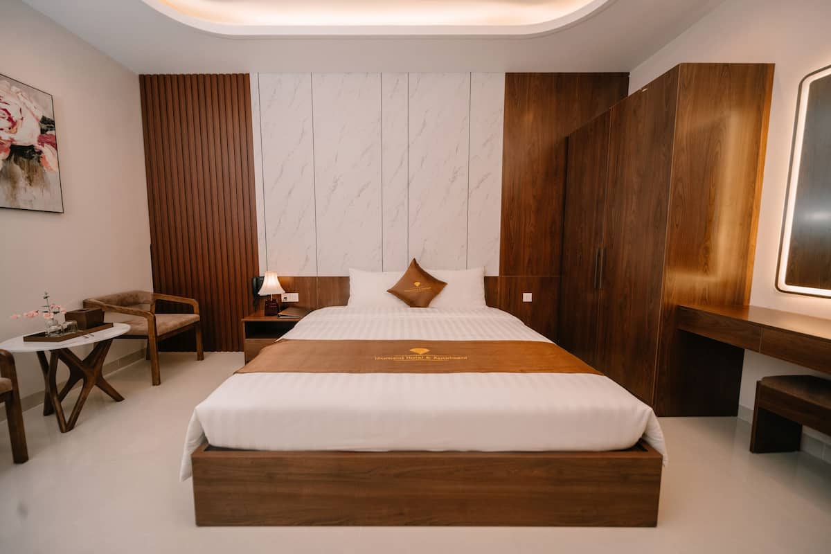 A modern hotel room with a large bed, wooden headboard, a desk, and a chair.
