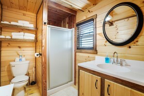 Baño de cabaña de madera con inodoro, lavamanos y ducha.
