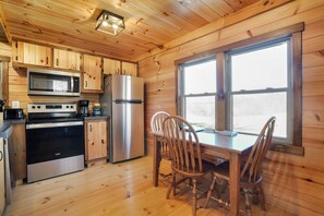 Een houten chalet van binnen met een keukenhoek, eettafel en stoelen.