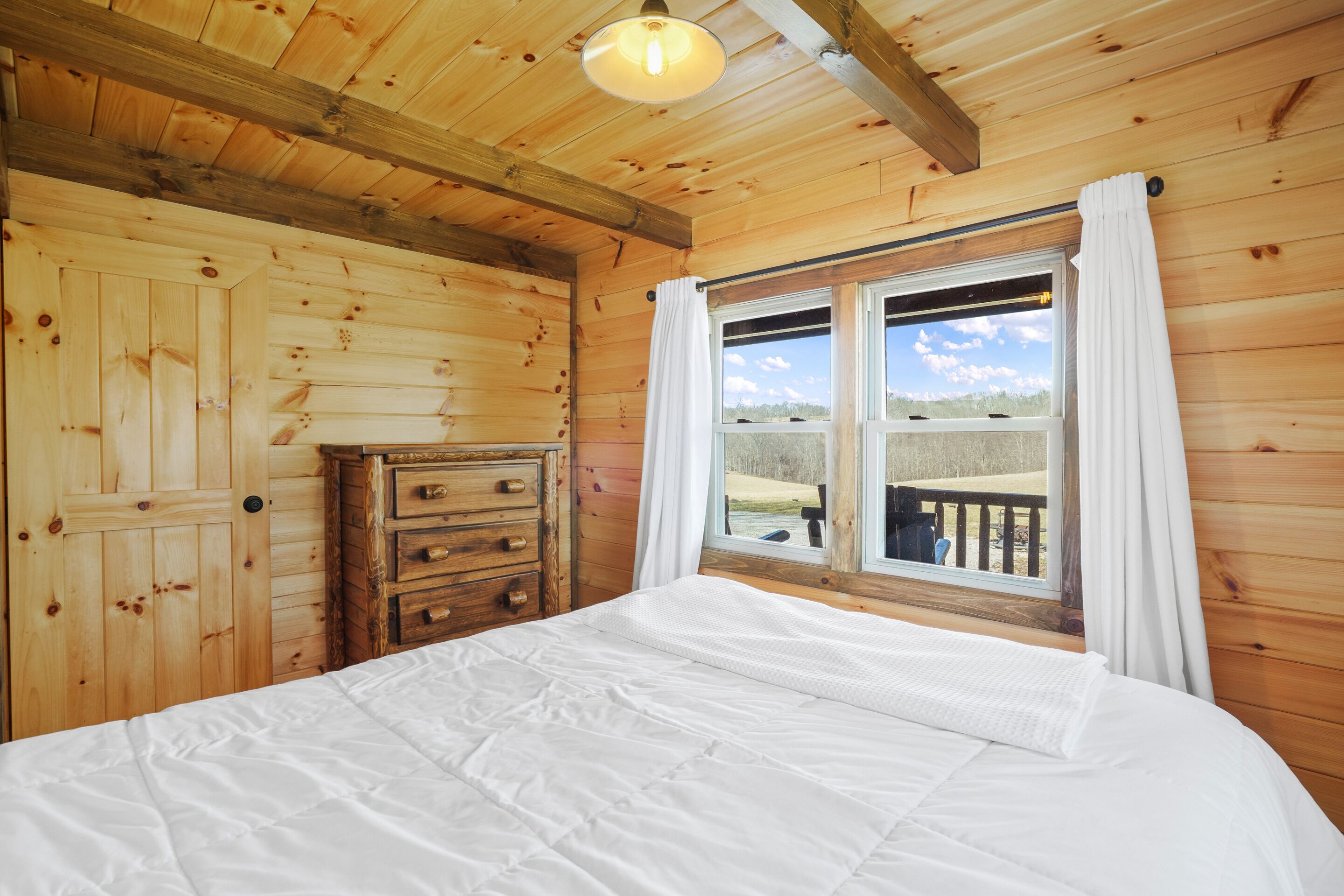 A wooden bedroom with a bed, a dresser, and a window with curtains.