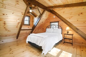 Un dormitorio de cabaña de madera con cama, mesita de noche y ventana.
