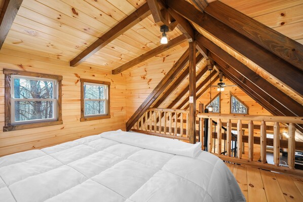 Un dormitorio de cabaña de madera con cama, ventanas y una escalera que lleva a un nivel superior.