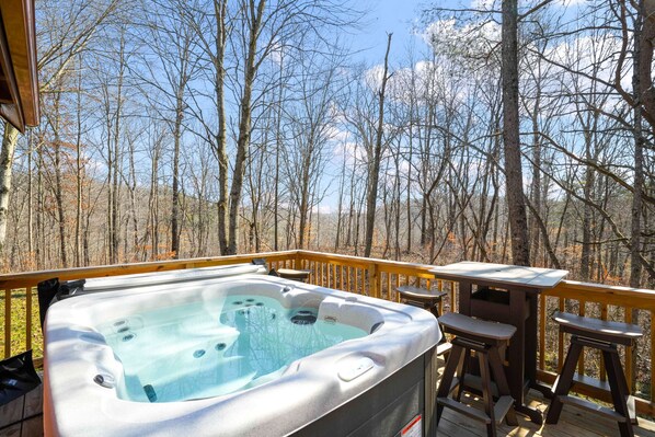 A hot tub on a wooden deck with a view of a forest.