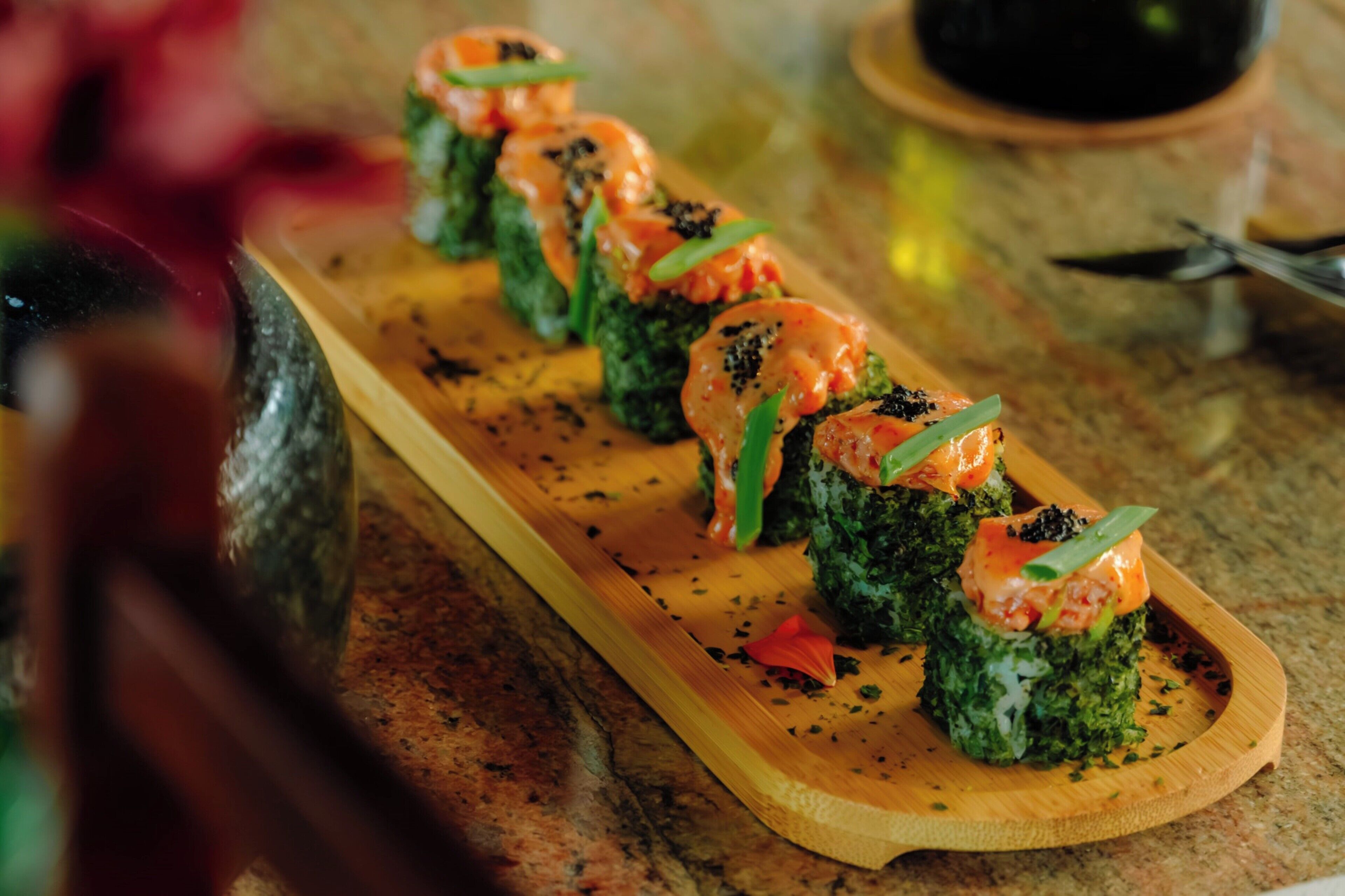 Una tabla de madera con rollos de sushi adornados con hojas verdes y salmón.