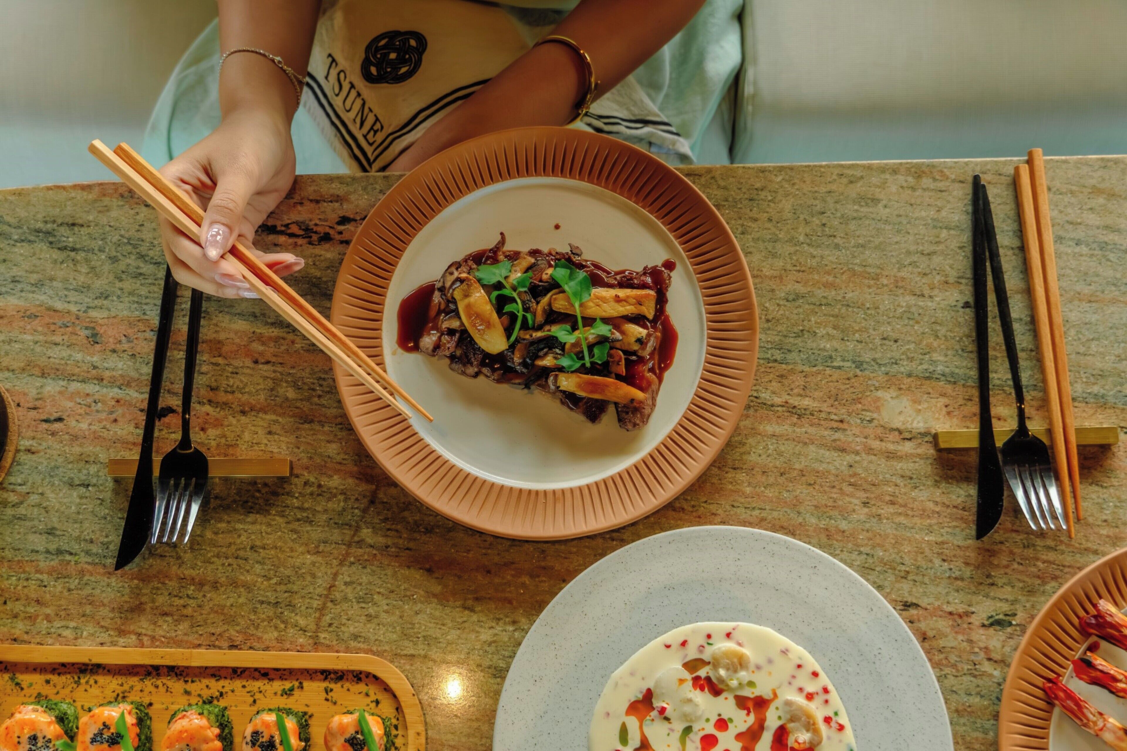 A dining table with a plate of food, chopsticks, and a fork.