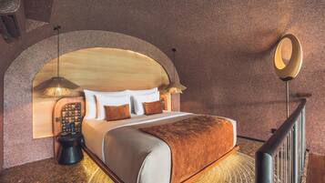 A hotel room with a large bed, a wooden headboard, a round mirror, and a small table with a lamp.