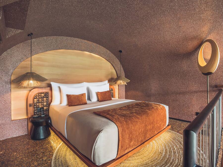 A hotel room with a large bed, a wooden headboard, a round mirror, and a small table with a lamp.