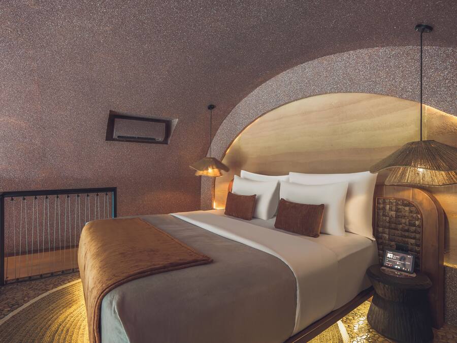 A hotel room with a large bed, a small side table, a lamp, and a unique arched ceiling.