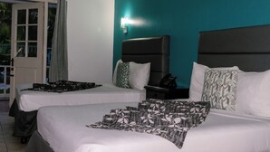 Une chambre d’hôtel avec deux lits, un mur d’accent de couleur turquoise et une porte-fenêtre coulissante donnant sur un espace extérieur.