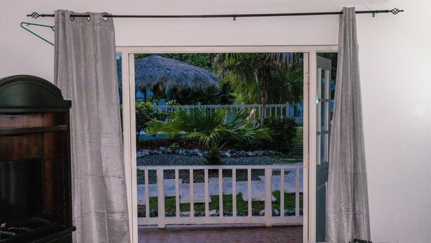 Une chambre dotée d’une télévision, d’un lit et offrant une vue sur un jardin agrémenté d’une structure au toit de chaume.