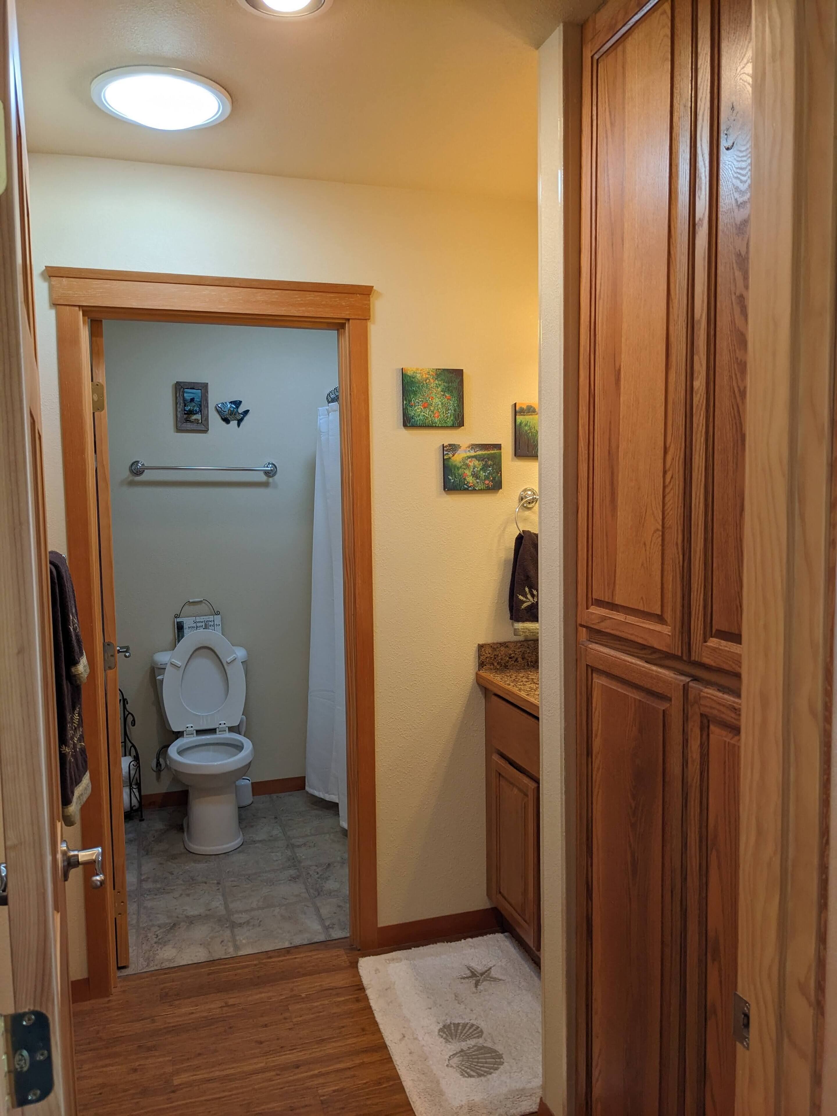 Une salle de bain avec des toilettes, des meubles en bois, un porte-serviettes et un petit tapis.