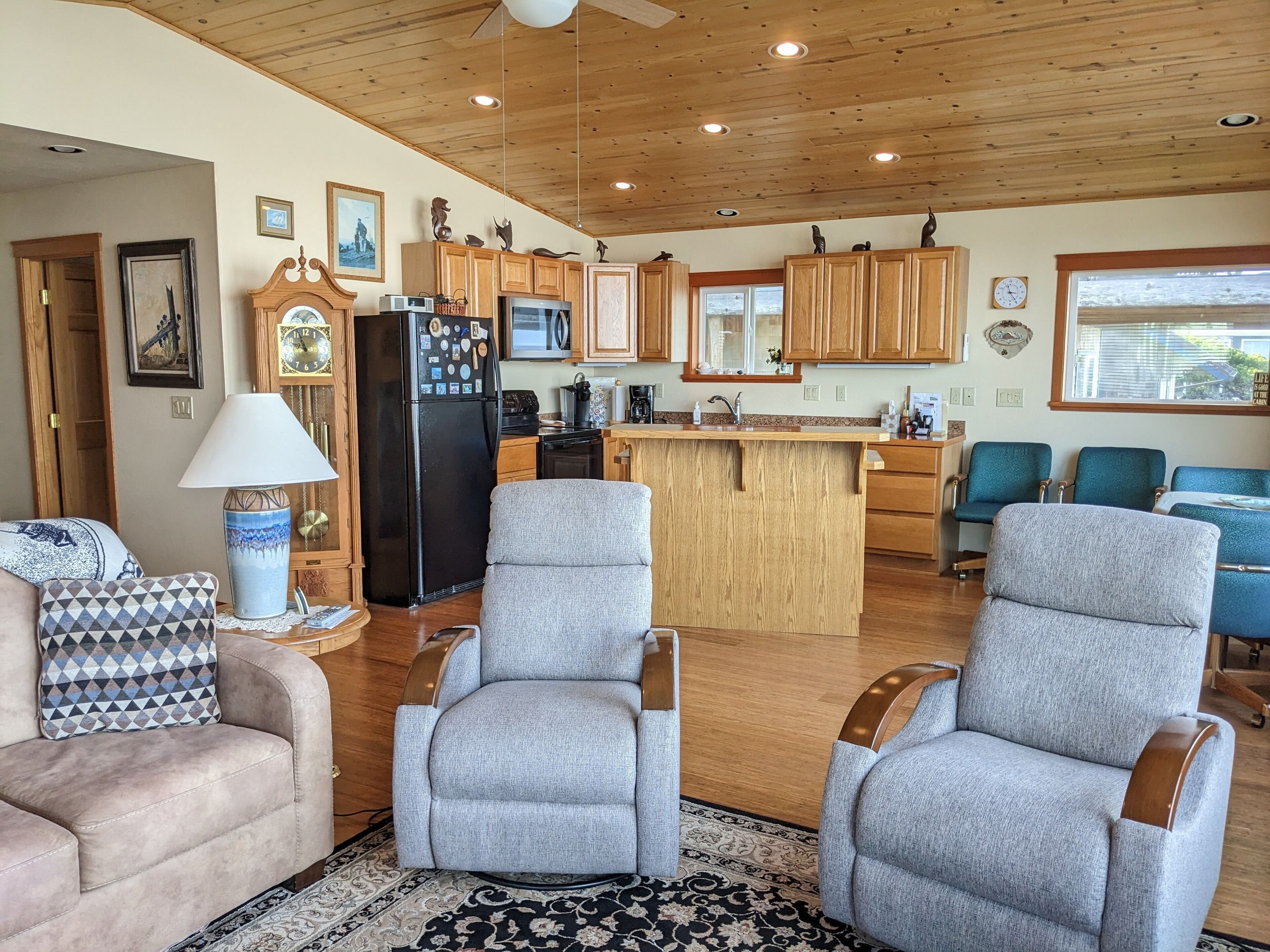 A spacious living area with a large gray sofa, two gray armchairs, and a wooden ceiling with recessed lighting.