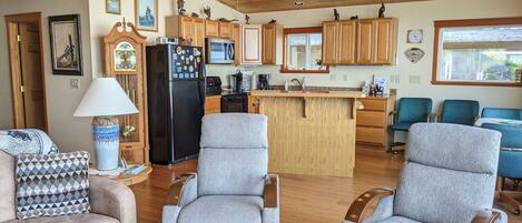 A spacious living area with a large gray sofa, two gray armchairs, and a wooden ceiling with recessed lighting.